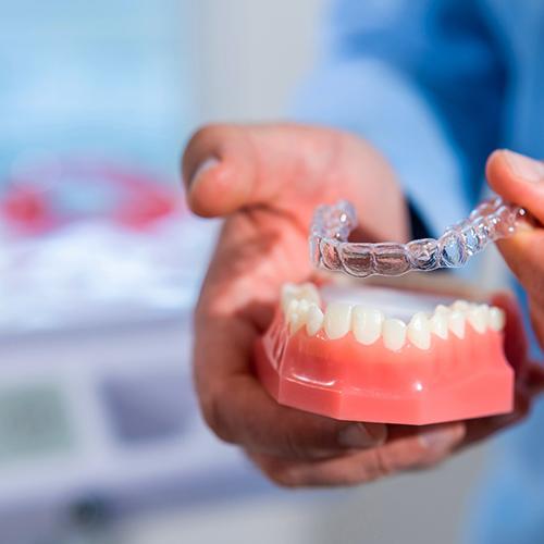 Patient placing clear aligner on model of teeth