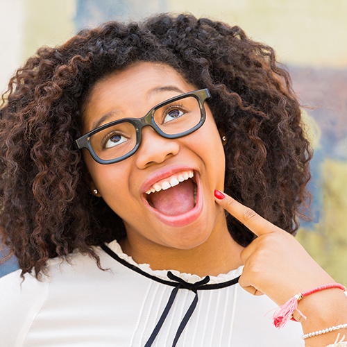 Woman pointing to smile after metal free dental crown placement