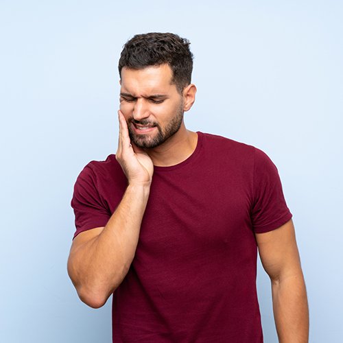 Bearded man rubbing his jaw in pain