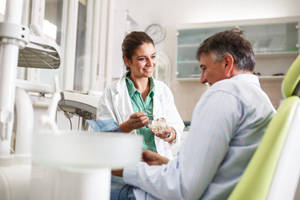 Smiling dentist showing patient model of teeth