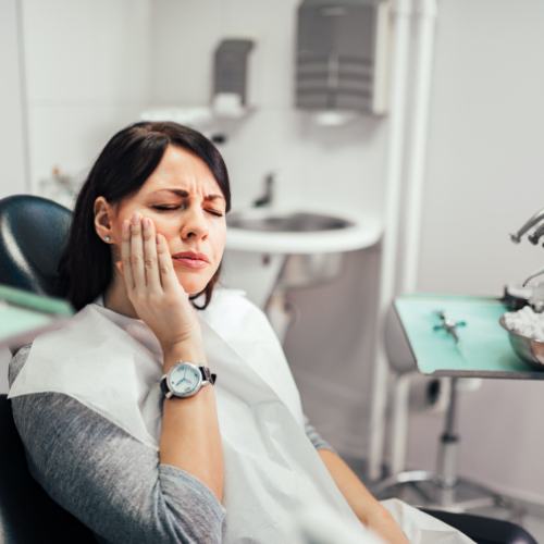 Woman holding cheek in dental chair before emergency dentistry treatment