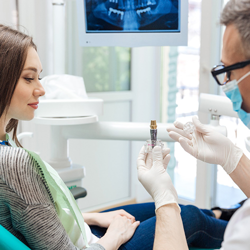 A male dentist showing his female patient a dental implant