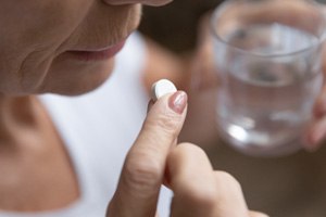 Senior woman with glass of water and painkiller pill