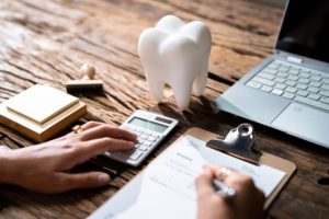 View of a desk that has a model of a tooth while someone calculates costs of an invoice on a calculator