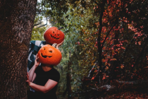 Two people wearing smiling pumpkins on their heads in the woods